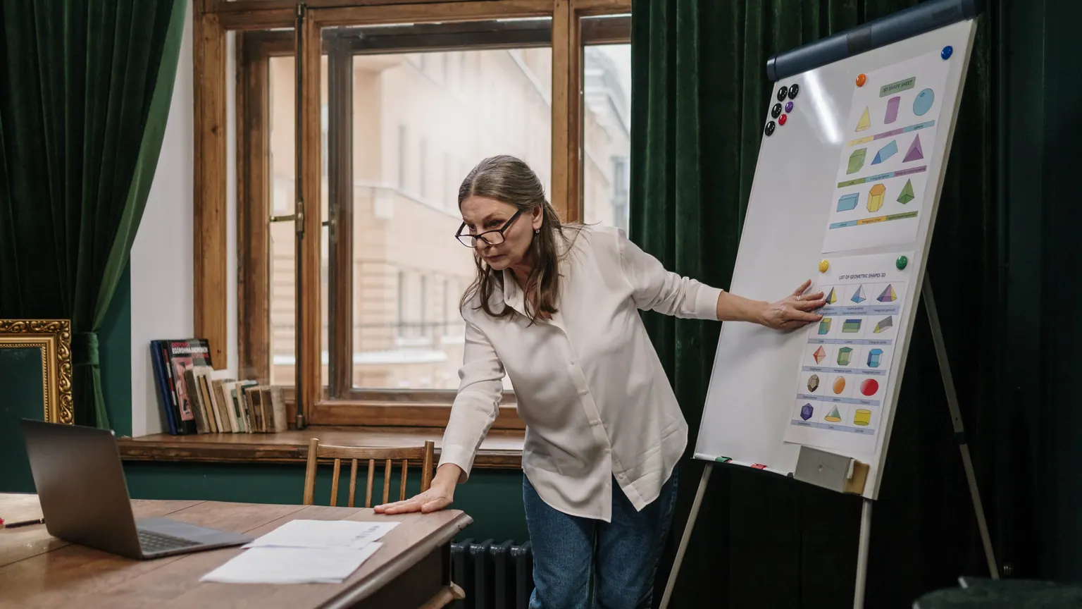 Professora aponta materiais visuais em um quadro durante o planejamento de aula