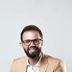 Retrato de Leandro Rodrigues sorrindo, de óculos e blazer.