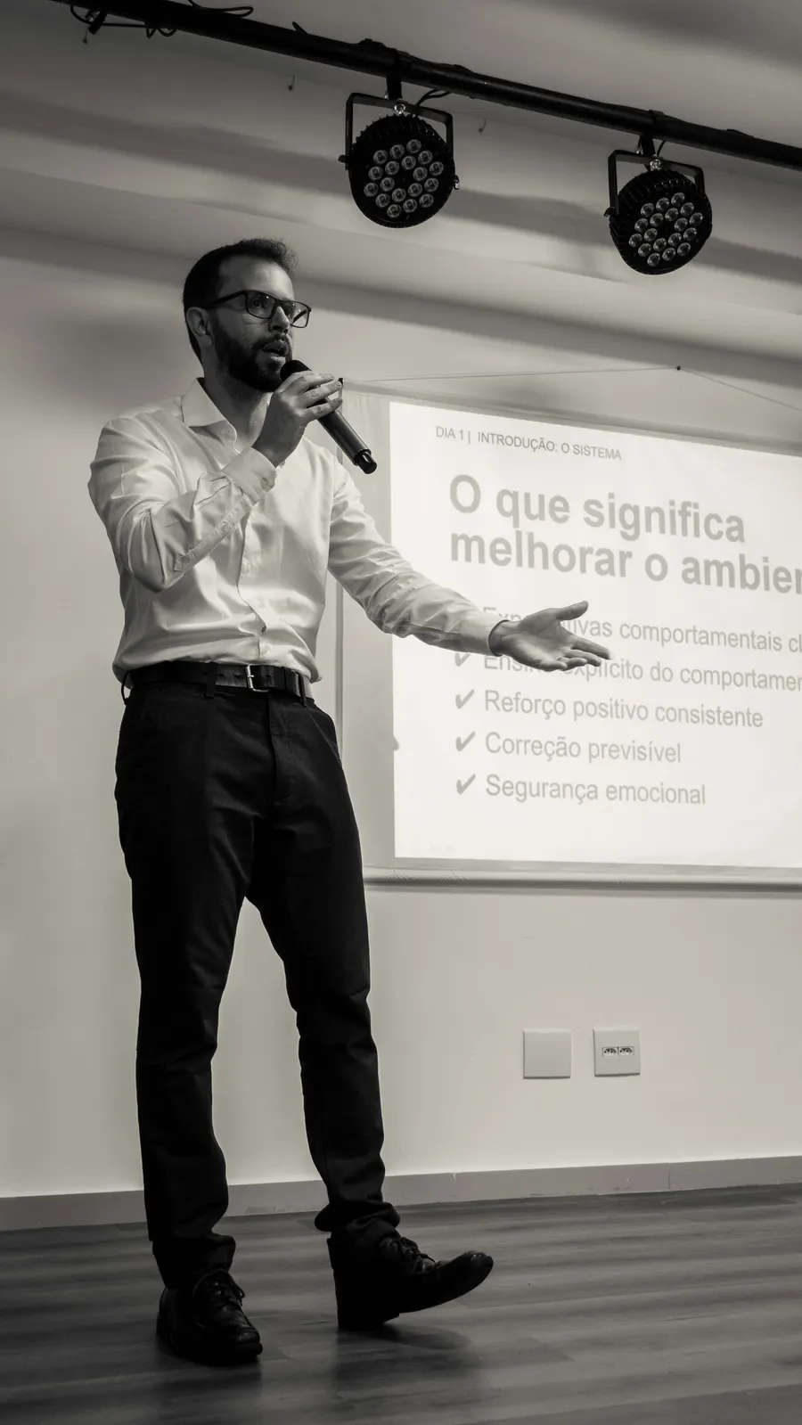 Leandro Rodrigues de microfone na mão, apresentando um slide sobre melhorar o ambiente de aprendizagem em formação presencial.